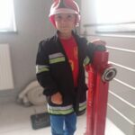 chłopiec w stroju strażaka stoi przy hydrancie