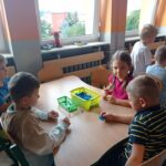 grupa dzieci siedzi przy stoliku i robi kulki z bibuły