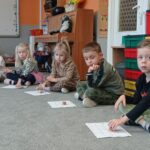 dzieci mają przed sobą karty pracy, w ręku pionki