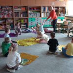 grupa dzieci na dywanie, nauczycielka stoi wskazuje na dzieci