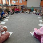 dzieci siedzą w kole, przed nimi karty pracy