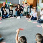 Dzieci siedzą na dywanie i podnoszą różową lub zieloną kartkę.