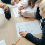 Dzieci siedzą przy stolikach i wypełniają karte pracy