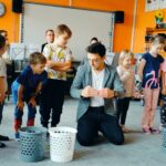 Dzieci stoją w rzędzie, prowadzący tłumaczy im ich zadanie