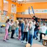 Dzieci wykonują gest oznaczający stop, trenerka trzyma nad nimi gąbkowe makarony