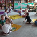 dzieci siedzą na dywanie, przed nimi kolorowe flagi