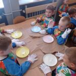 grupa dzieci siedzi przy stolikach, są ubrani w rękawiczki