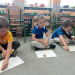 troje chłopców trzyma pionki i przesuwają po kartach pracy