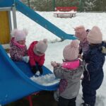 dzieci stoją obok zaśnieżonej zjeżdżalni