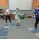 troje dzieci stoi na dywanie, jedno rzuca kostką