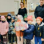 Dzieci pozują do zdjęcia z paczką herbat oraz dorosłymi z DPS