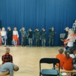 Dzieci siedzą na ławkach i oglądają występ.