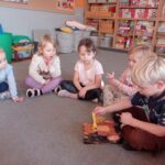 kilkoro dzieci siedzi na dywanie, chłopiec karmi misia