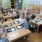 dzieci siedzą przy stolikach i wyklejają obrazki