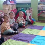 grupa chłopców siedzi przed kolorowym dywanem, chłopiec rzuca kostką