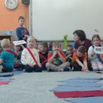 pani z grupą dzieci, przed nimi pola gry zrobione z materiałowych prostokątów