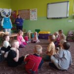 dzieci siedzą na dywanie, do sali wchodzi Kicia Kocia i pracownik księgarni