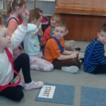 grupa dzieci siedzi na dywanie, dziewczynka zgłasza się