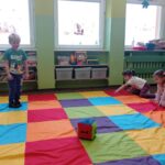 chłopiec stoi na kolorowym dywanie, przed nim leży kostka