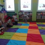 dziewczynka skacze po kolorowych polach, grupa dzieci patrzy