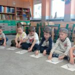 dzieci siedzą na dywanie, przed nimi obrazek bombki