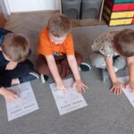 dzieci siedzą na dywanie, wodzą palcem po obrazku