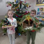 dwoje dzieci stoi przed choinką, trzyma w ręku prace wykonane na konkurs