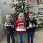 troje dzieci stoi przed choinką, trzyma w ręku prace wykonane na konkurs