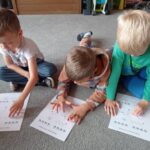 dzieci siedzą na dywanie, wodzą palcem po obrazku