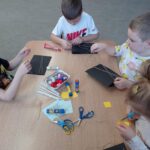 dzieci przy stoliku wycinają elementy prac